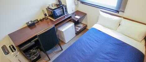 A hotel room with a bed, a desk with a computer, a microwave, a coffee maker, and a small refrigerator.