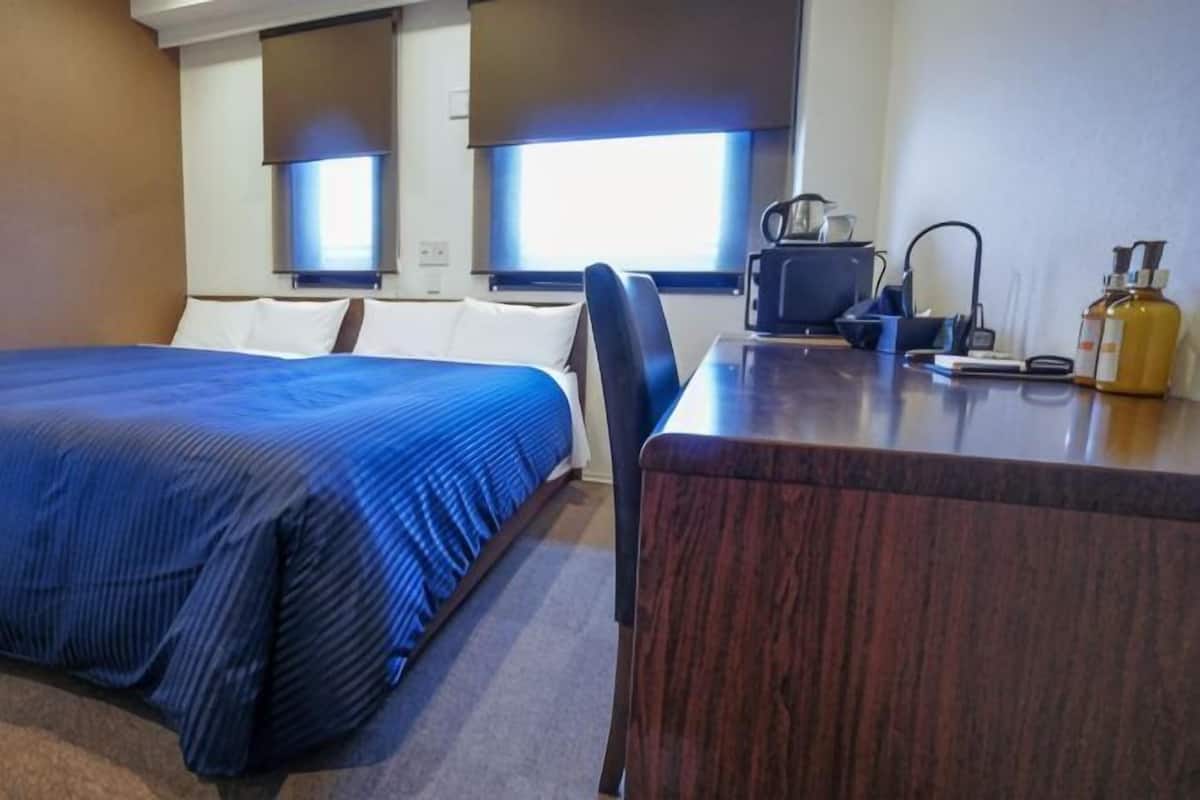 Ein Hotelzimmer mit einem Bett, einem Schreibtisch, einem Stuhl, einer Lampe und einer Flasche auf dem Schreibtisch.