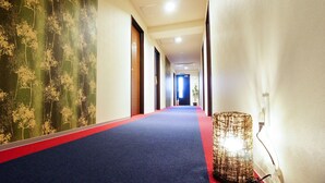 Un couloir d’hôtel avec un tapis bleu, un séparateur de tapis rouge et un mur orné d’un motif d’arbre.