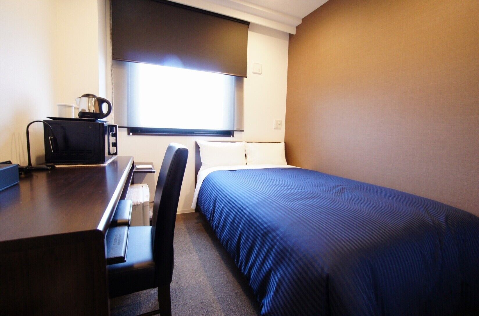 Ein Hotelzimmer mit Bett, Schreibtisch, Stuhl, Kaffeemaschine und Fenster.