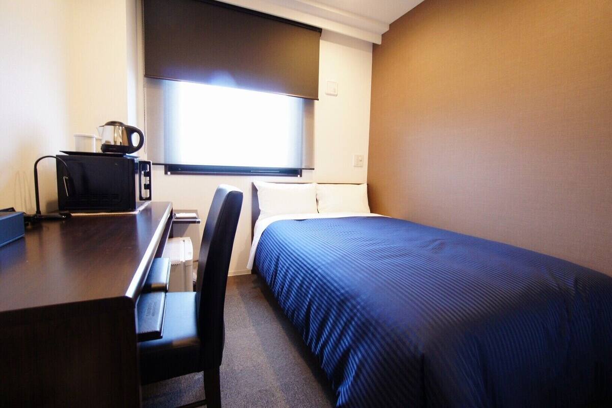 Een hotelkamer met een bed, een bureau, een stoel, een koffiezetapparaat en een raam.