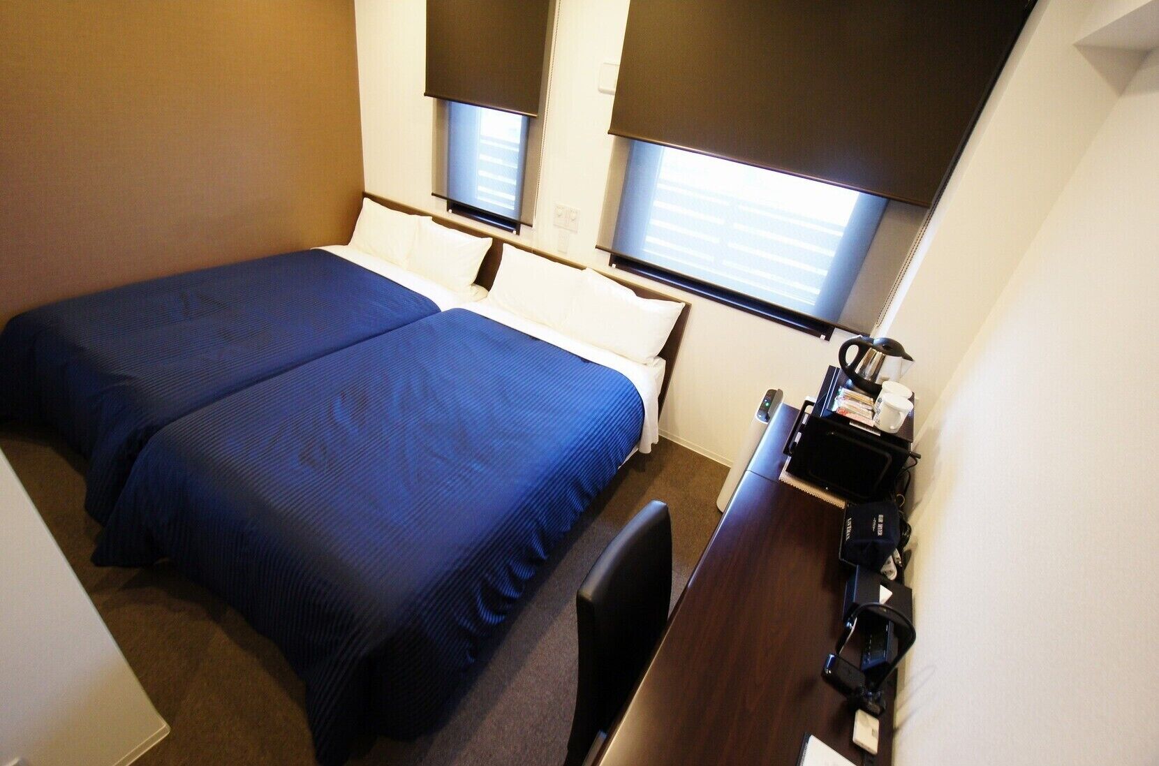 Ein Hotelzimmer mit zwei Betten, einem Schreibtisch und einem Fenster mit Jalousien.