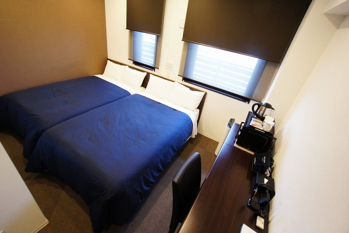 Habitación de hotel con dos camas, un escritorio y una ventana con persianas.