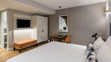 Une chambre d’hôtel moderne dotée d’un grand lit, d’un coin salon avec une table et des chaises, d’un téléviseur fixé au mur et d’un tableau au-dessus de la table.