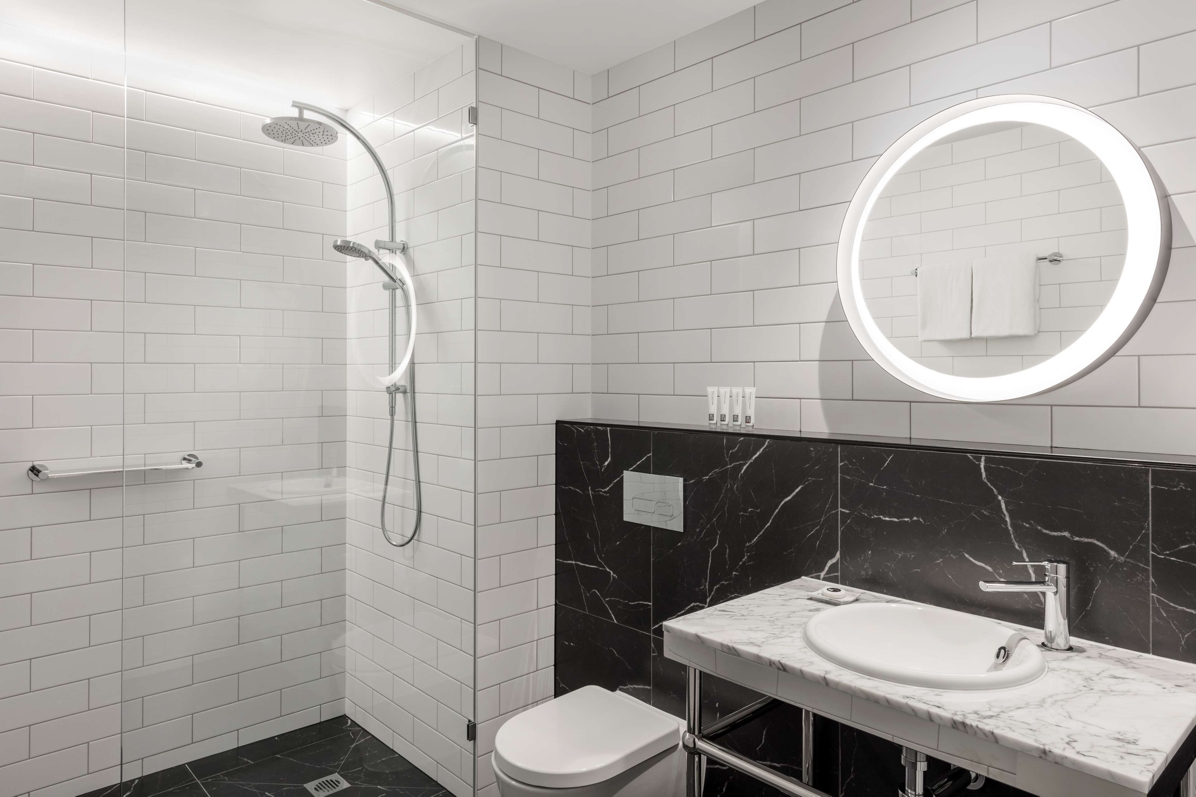 A modern bathroom with white subway tiles, a black marble backsplash, a white sink, and a shower with a curved glass door.