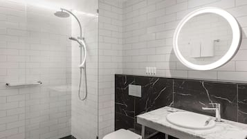 A modern bathroom with white subway tiles, a black marble backsplash, a white sink, and a shower with a curved glass door.