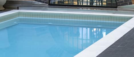 A swimming pool with a tiled edge, a brick wall, and a metal arch structure.