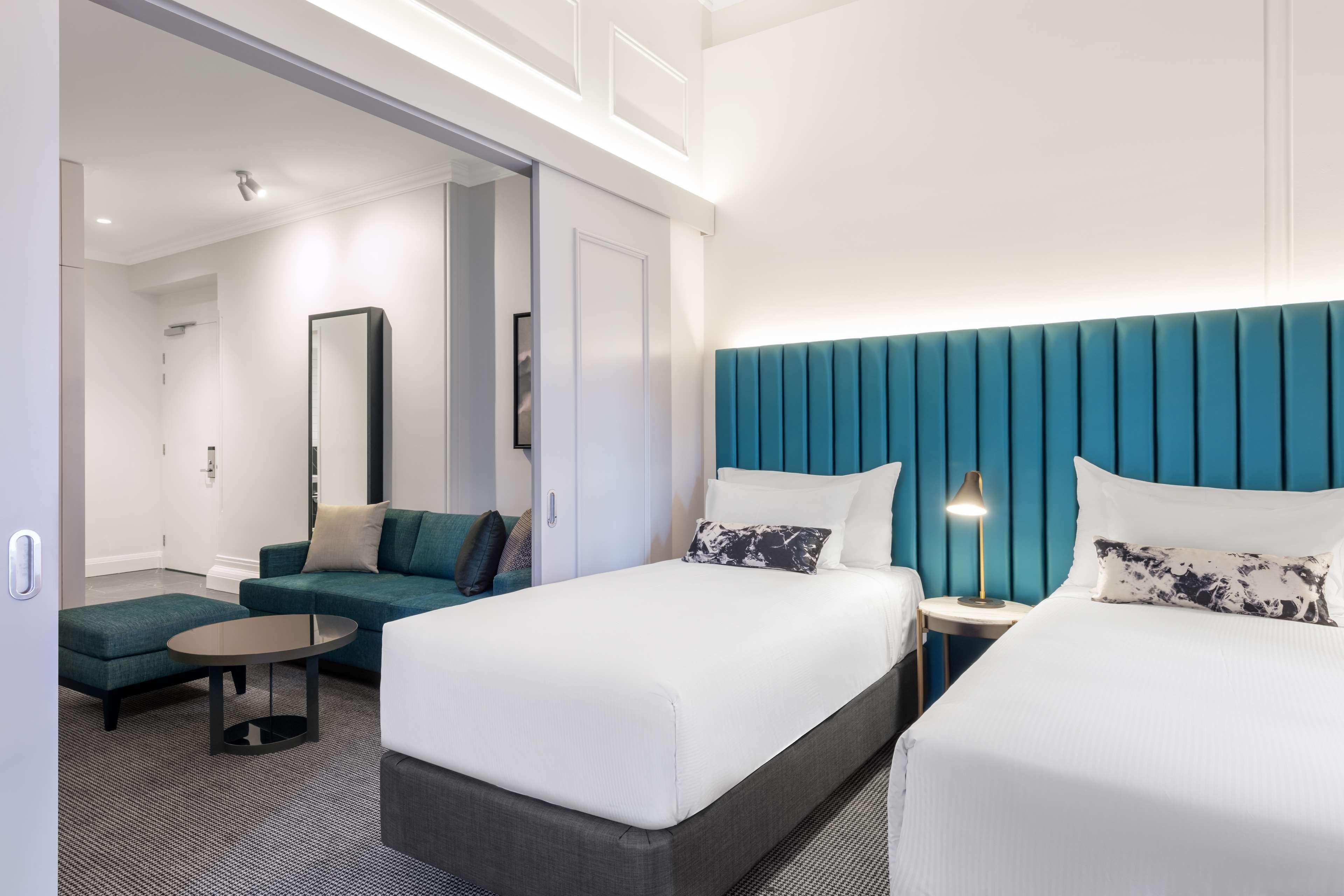 Een moderne hotelkamer met twee bedden, een sofa, een tafeltje en een spiegel.
