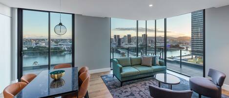 A spacious room with a large window offering a city view, a dining table with chairs, a sofa, and a small coffee table.