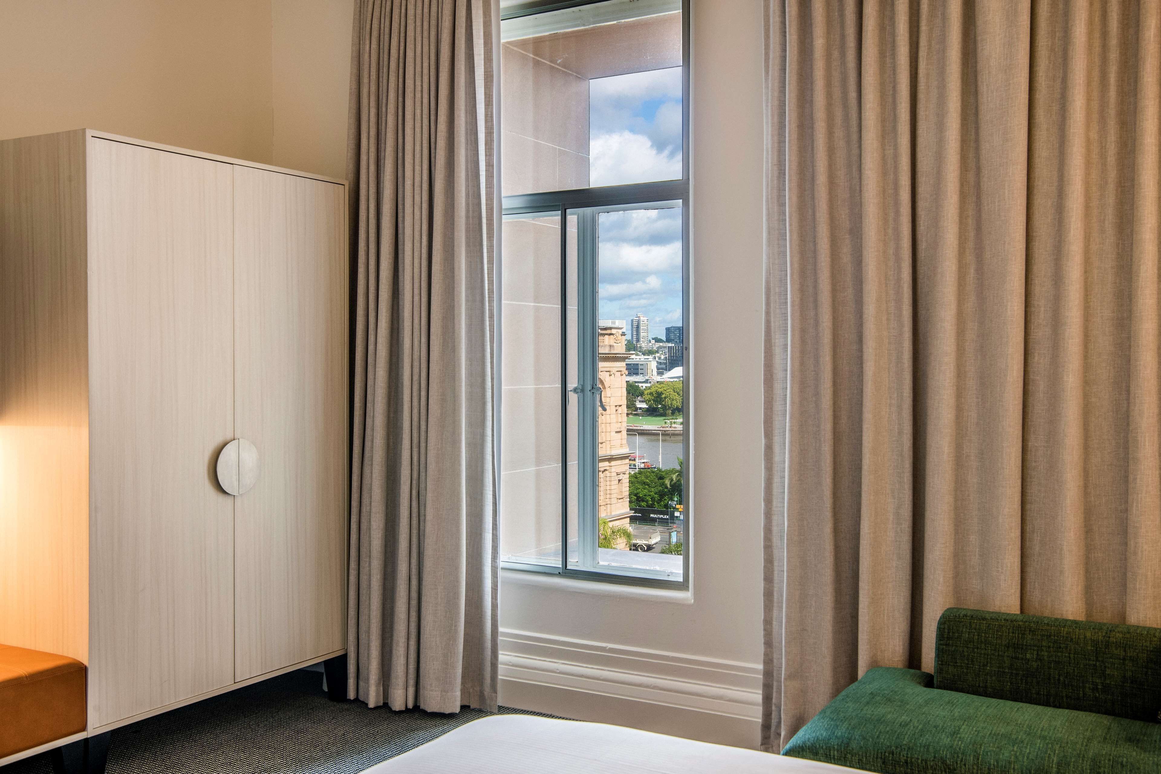 A hotel room with a bed, a green sofa, a wardrobe, and a window with a city view.