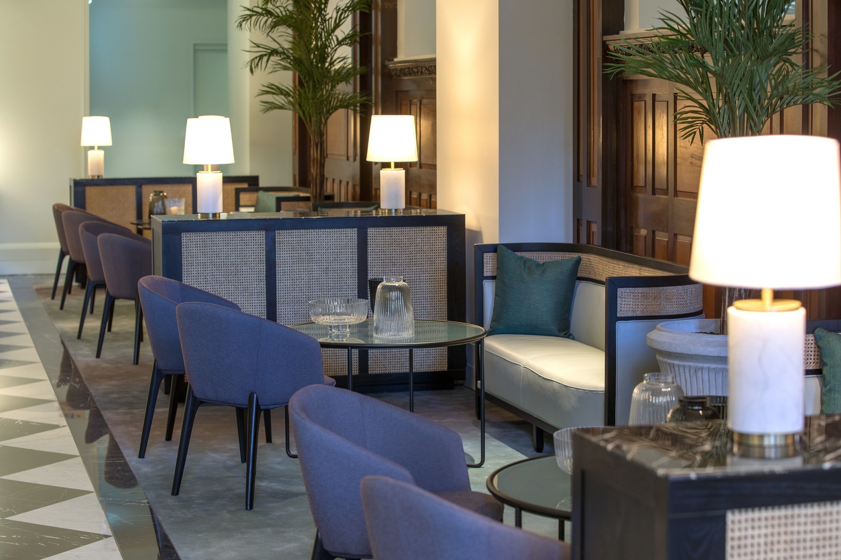 A hotel lobby with seating arrangements, including chairs and sofas, and tables with lamps.