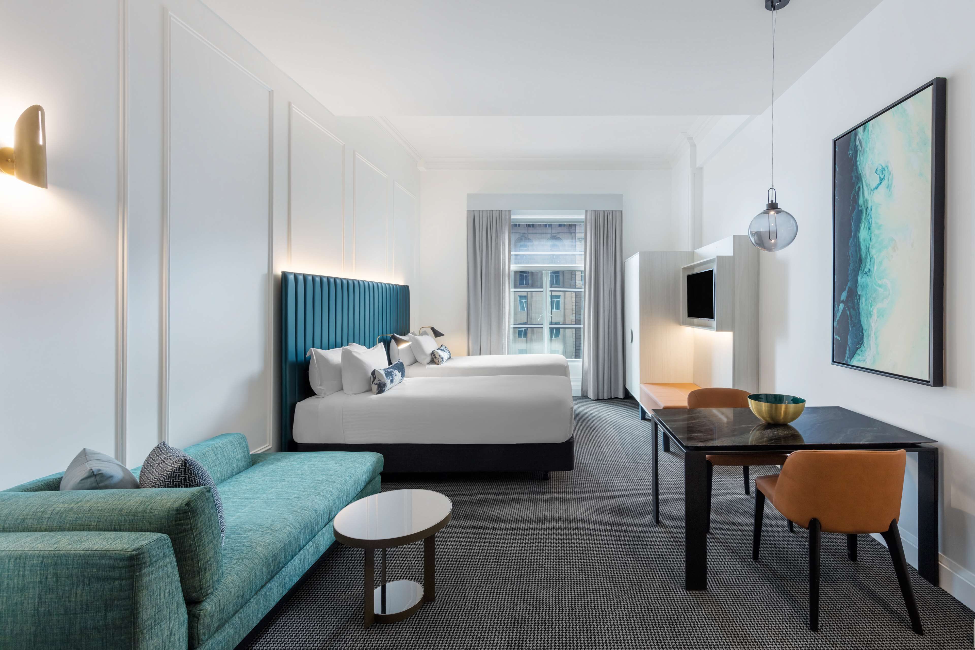 A hotel room with a bed, a sofa, a dining table, and a TV.