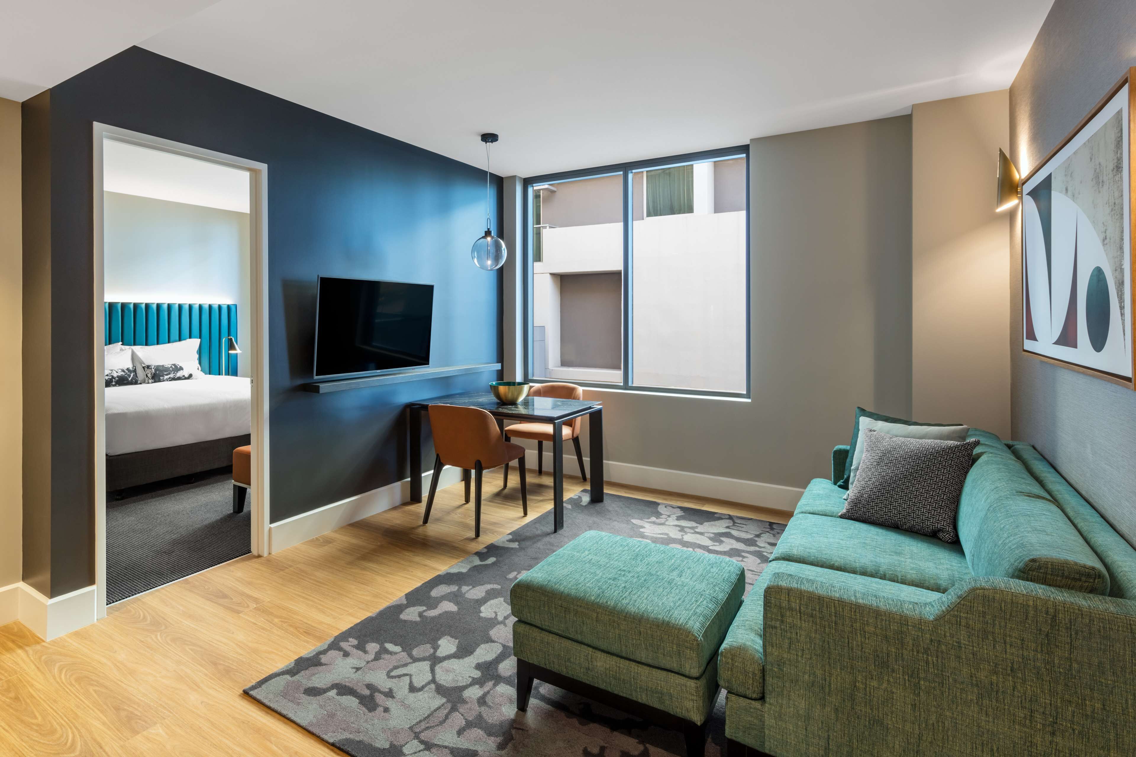 A modern hotel room with a bed, a TV, a dining area, and a sofa.