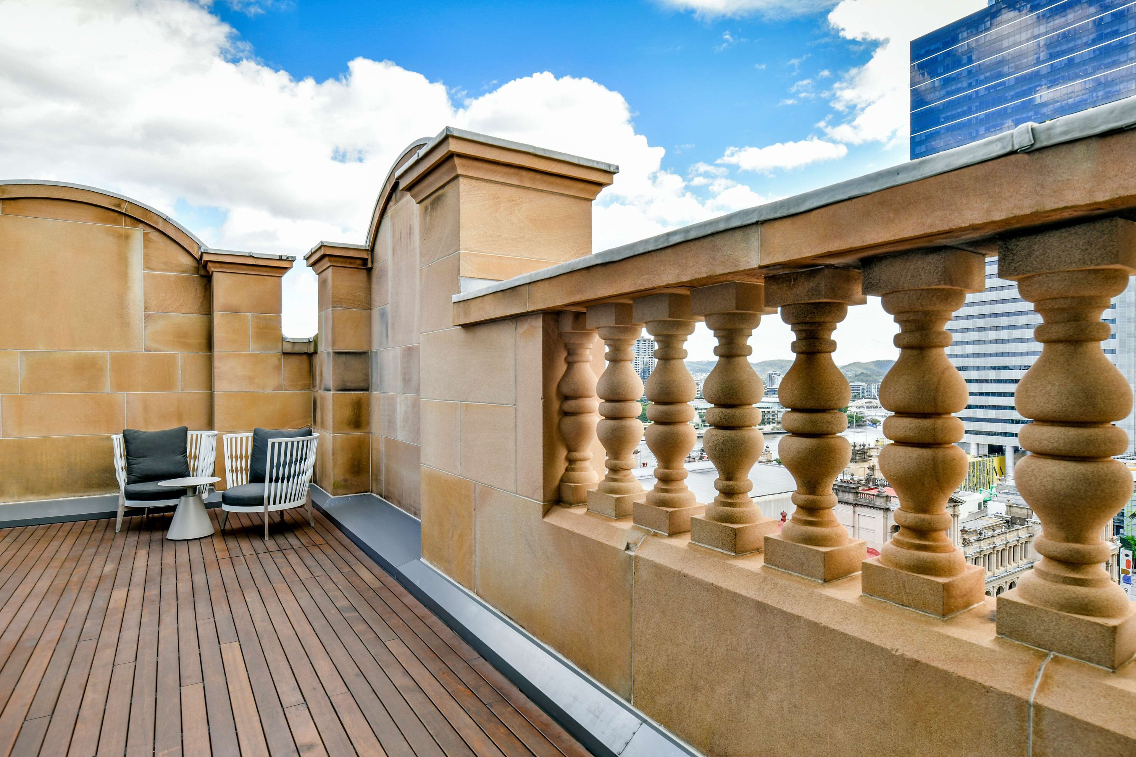 Eine Dachterrasse mit Holzdeck, zwei weißen Stühlen mit Kissen und einem kleinen Tisch.