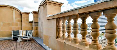 Eine Dachterrasse mit Holzdeck, zwei weißen Stühlen mit Kissen und einem kleinen Tisch.