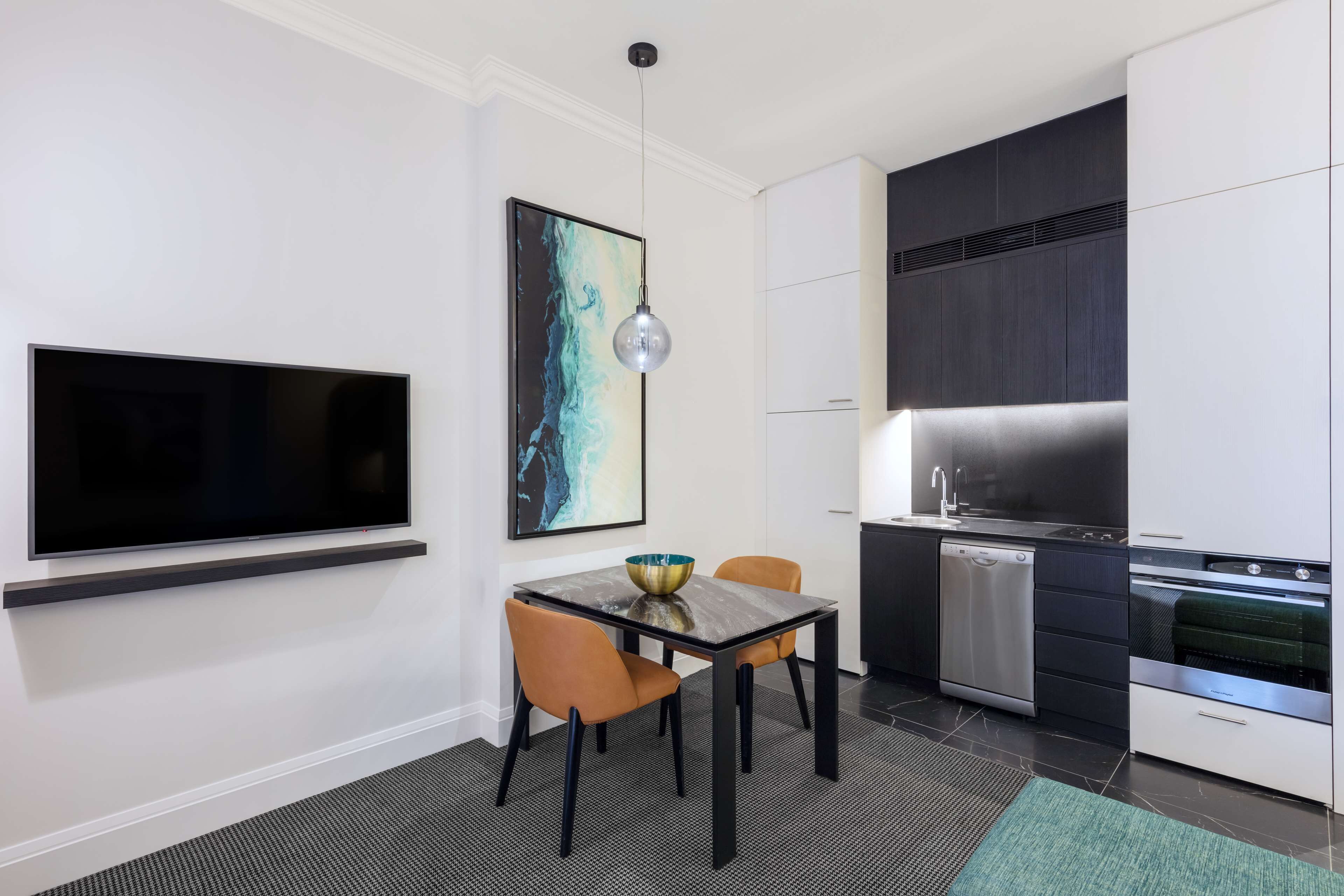 A modern kitchen with a flat-screen TV, a dining table with chairs, and a large painting on the wall.