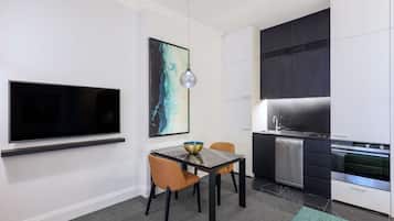 A modern kitchen with a flat-screen TV, a dining table with chairs, and a large painting on the wall.