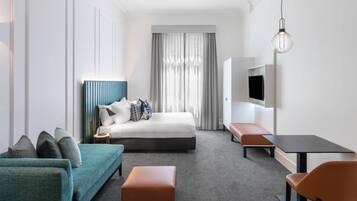 A modern hotel room with a bed, a sofa, a table, and a TV.