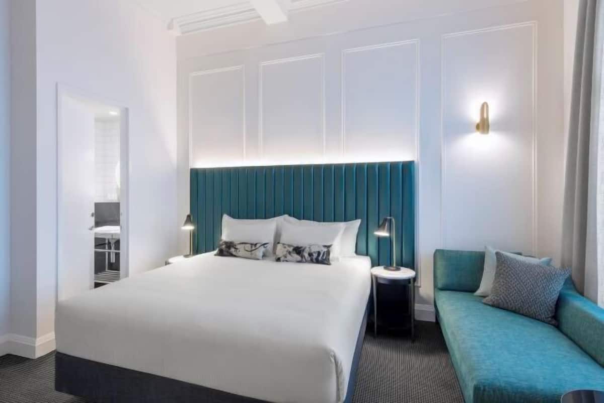 A hotel room with a bed, a nightstand, a sofa, and a wall-mounted light.