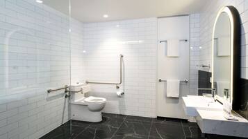 Un baño moderno con paredes de azulejos blancos, suelo de mármol negro, inodoro blanco, lavabo con espejo y barandilla.
