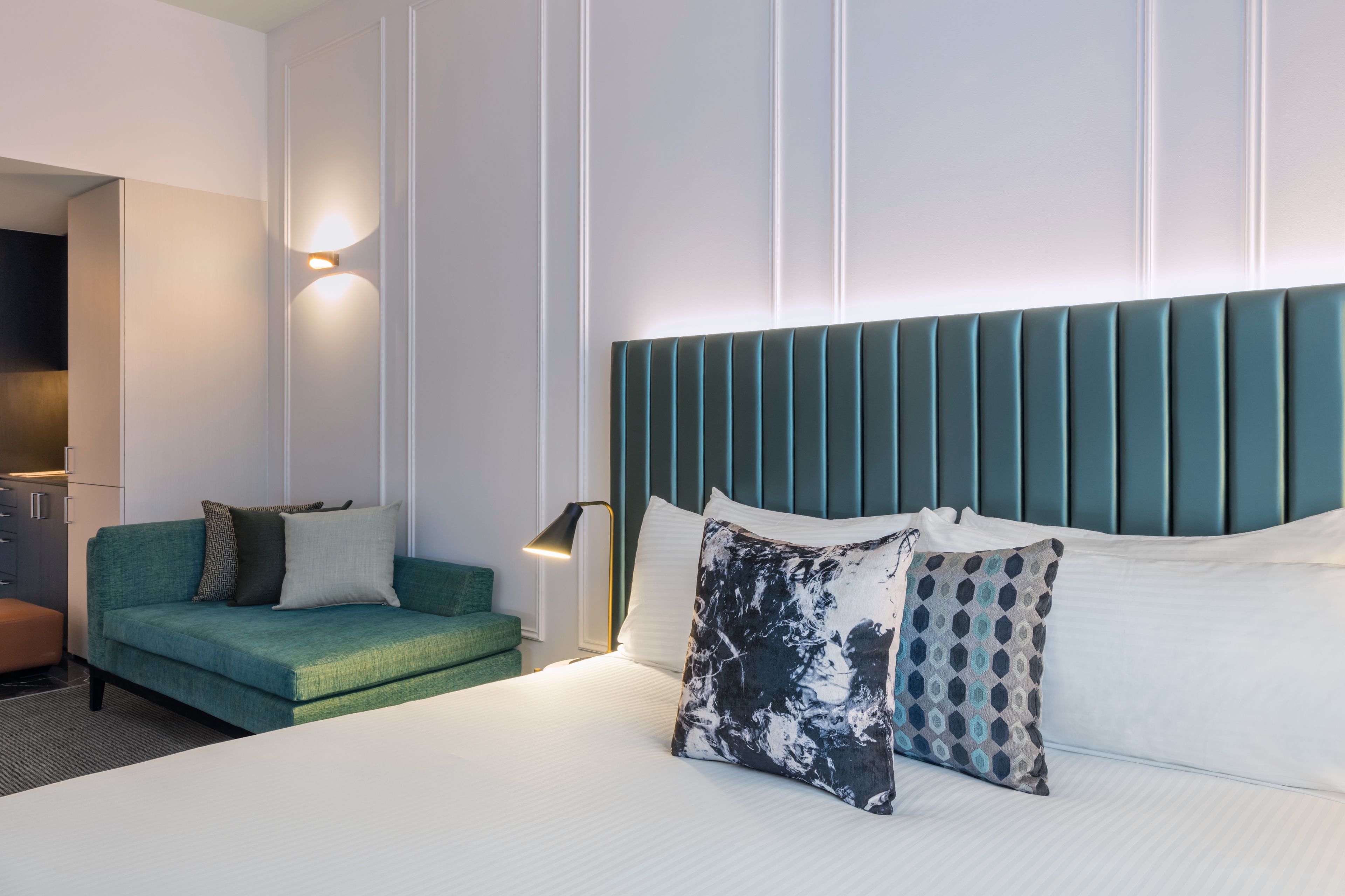 A modern hotel room with a large bed, a green sofa, and a nightstand with a lamp.
