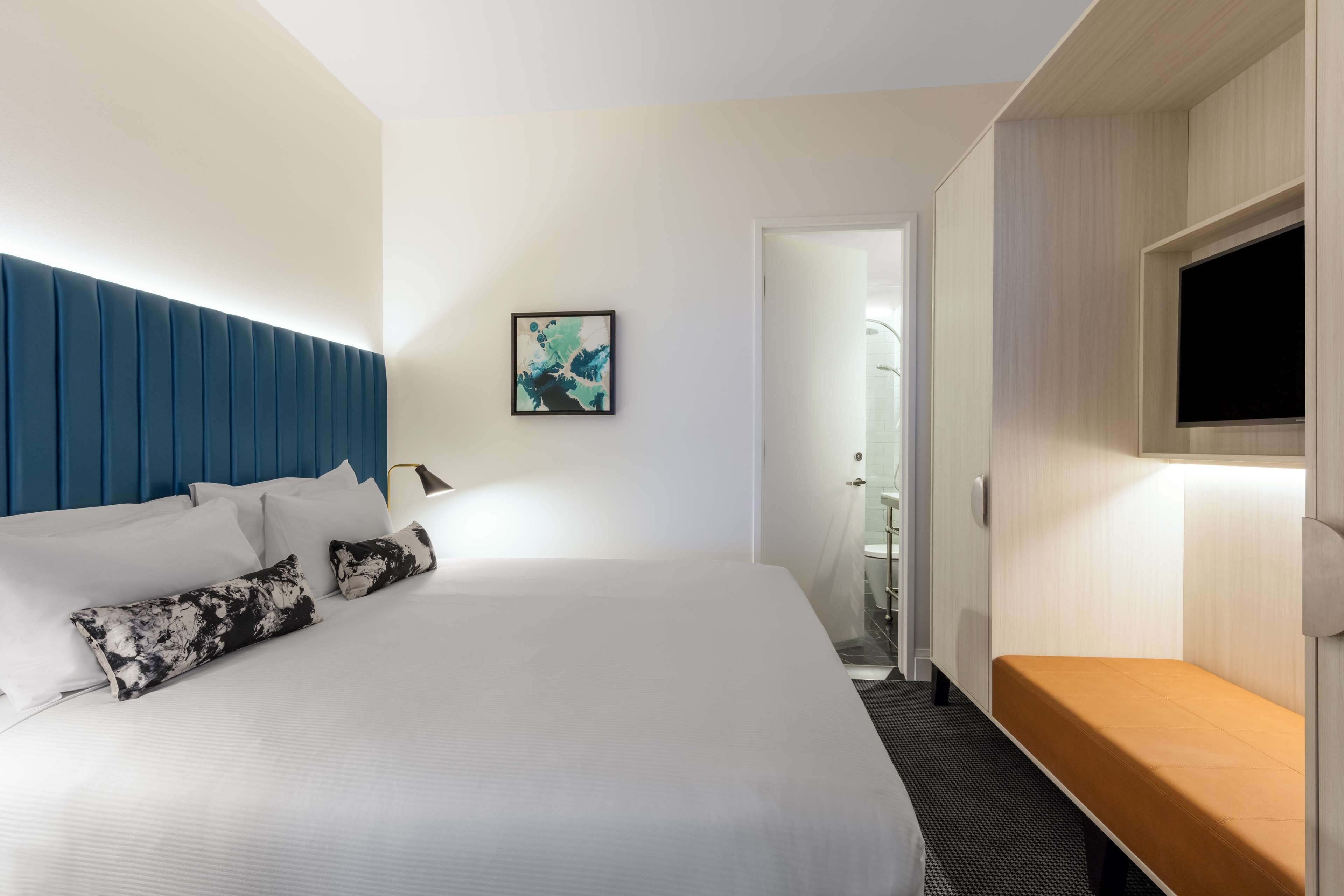 Una habitación de hotel moderna con una cama grande, un banco de madera, un televisor de pantalla plana y una obra de arte enmarcada en la pared.