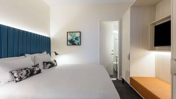 Una habitación de hotel moderna con una cama grande, un banco de madera, un televisor de pantalla plana y una obra de arte enmarcada en la pared.