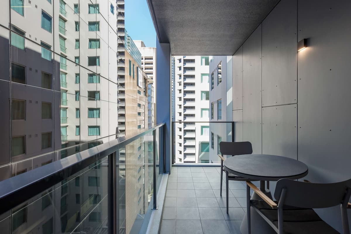 A balcony with a table and chairs, overlooking a cityscape with modern buildings.