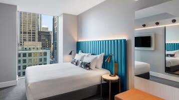 Una habitación de hotel moderna con una cama grande, una mesita de noche, un espejo y vistas a la ciudad.