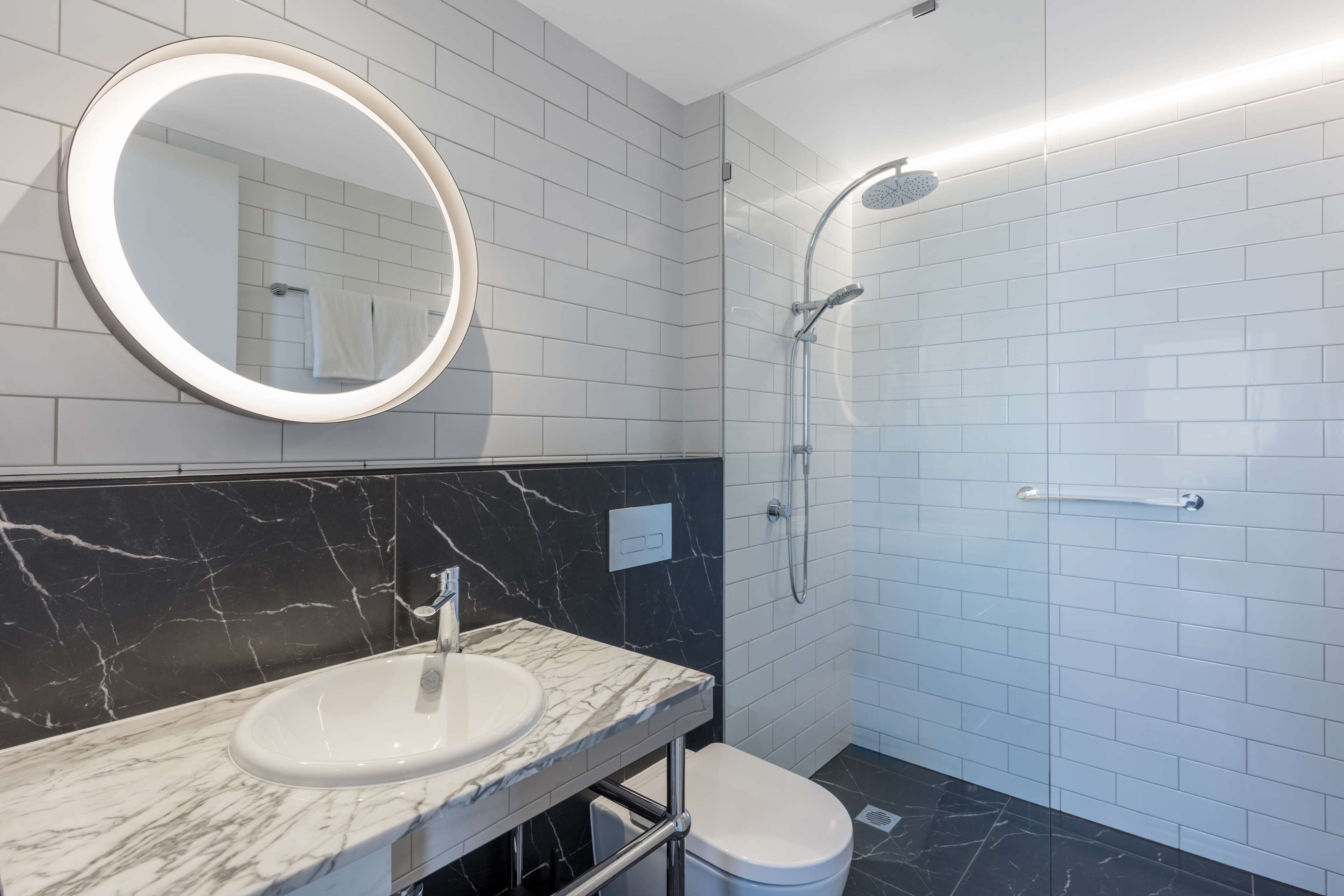 Un baño moderno con un lavabo blanco, encimera de mármol negro y ducha con puerta de vidrio.