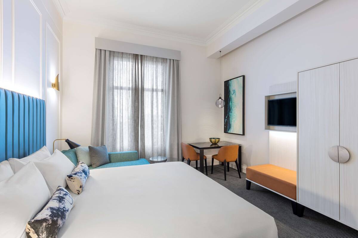 A hotel room with a large bed, a desk, a chair, a small table, and a TV.