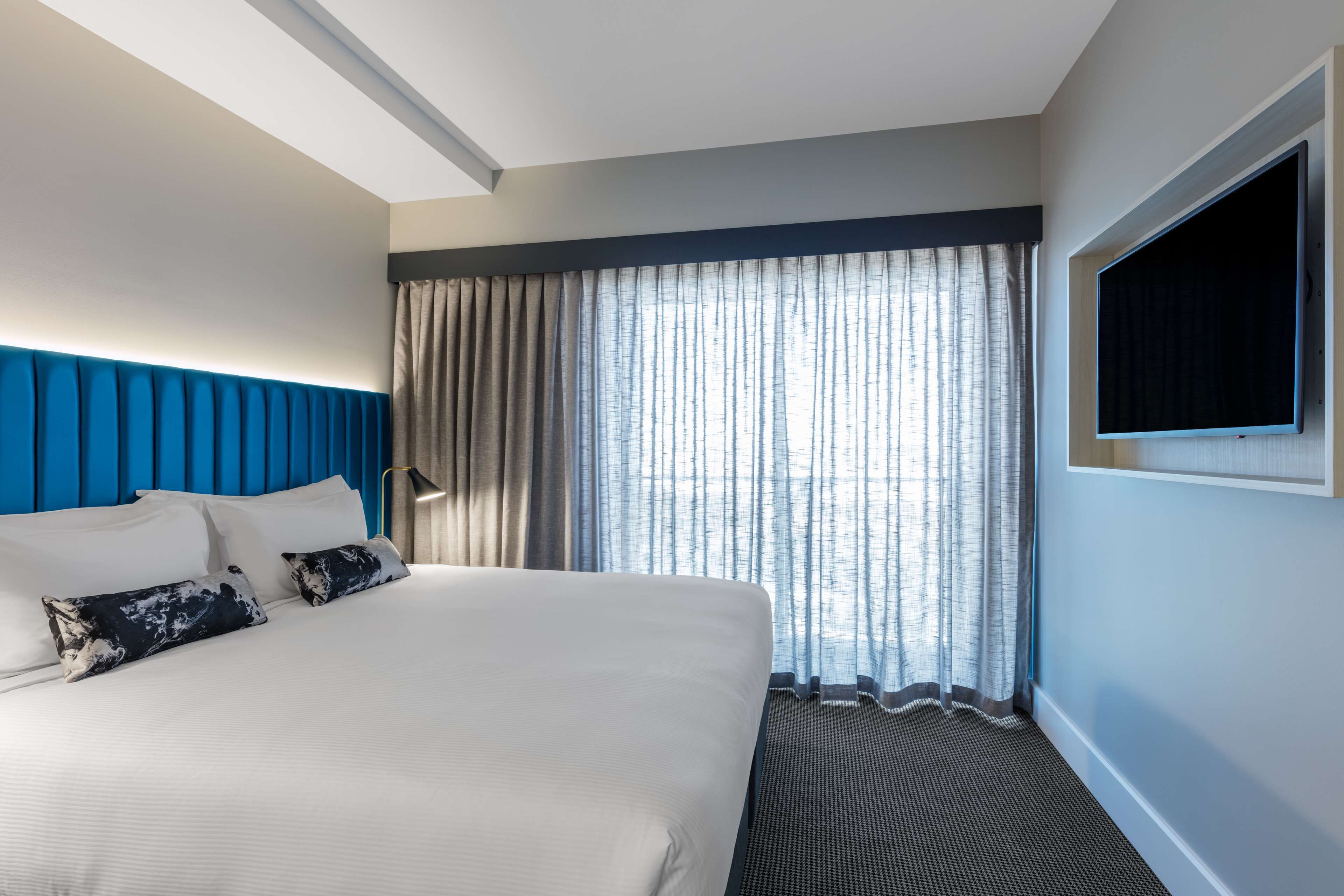 Ein Hotelzimmer mit einem großen Bett, einem an der Wand befestigten Fernseher und einem Fenster mit Vorhängen.