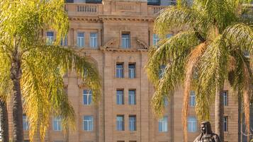 A hotel with a modern facade, a statue in front, and palm trees around.