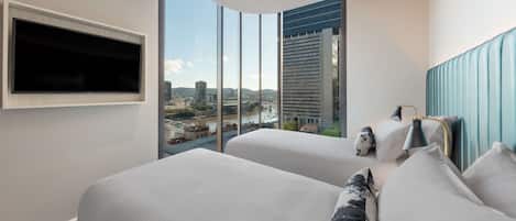 Habitación de hotel con dos camas, un televisor montado en la pared y un amplio ventanal con vistas a la ciudad.