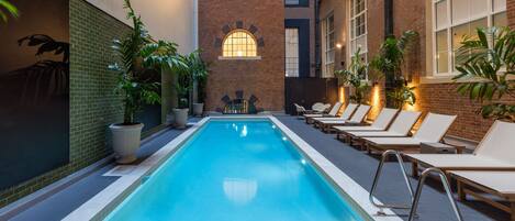 A pool area with lounge chairs and potted plants, surrounded by brick walls and windows.