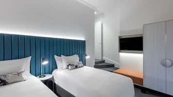 A modern hotel room with two beds, a TV, a wardrobe, and a bench.