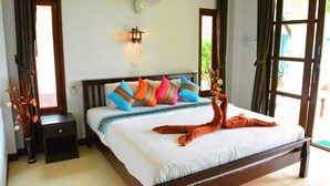 A neatly made bed with colorful pillows, a bedside table, a wall-mounted fan, and a window with curtains.
