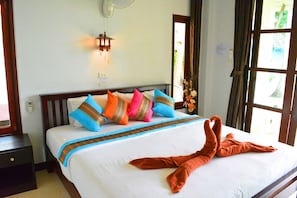 A neatly made bed with colorful pillows, a wooden headboard, and a towel arranged in a heart shape.