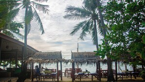 A beachside setting with thatched-roof structures, wooden tables, and chairs.