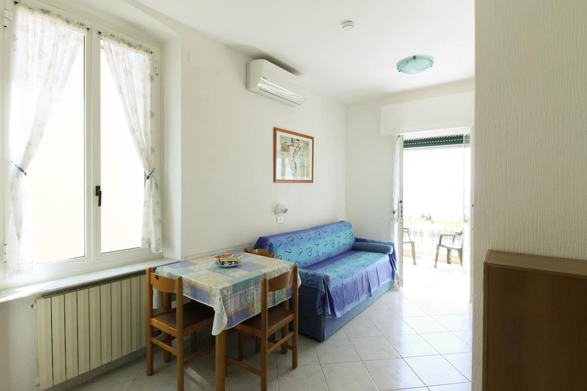 A dining area with a table and chairs, a sofa, a radiator, and a window with curtains.