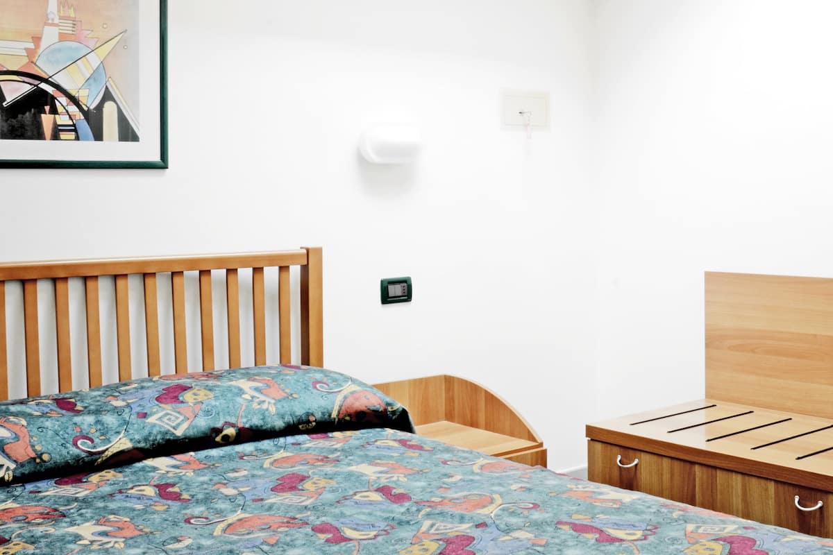 A bedroom with a skylight, a bed with patterned bedding, a wooden headboard, a bedside table, and a wall-mounted light.