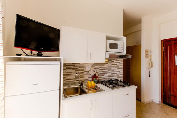 A compact kitchen with white cabinetry, a built-in microwave, a gas stove, and a flat-screen TV. - Residence Villa Alda (Pietra Ligure)