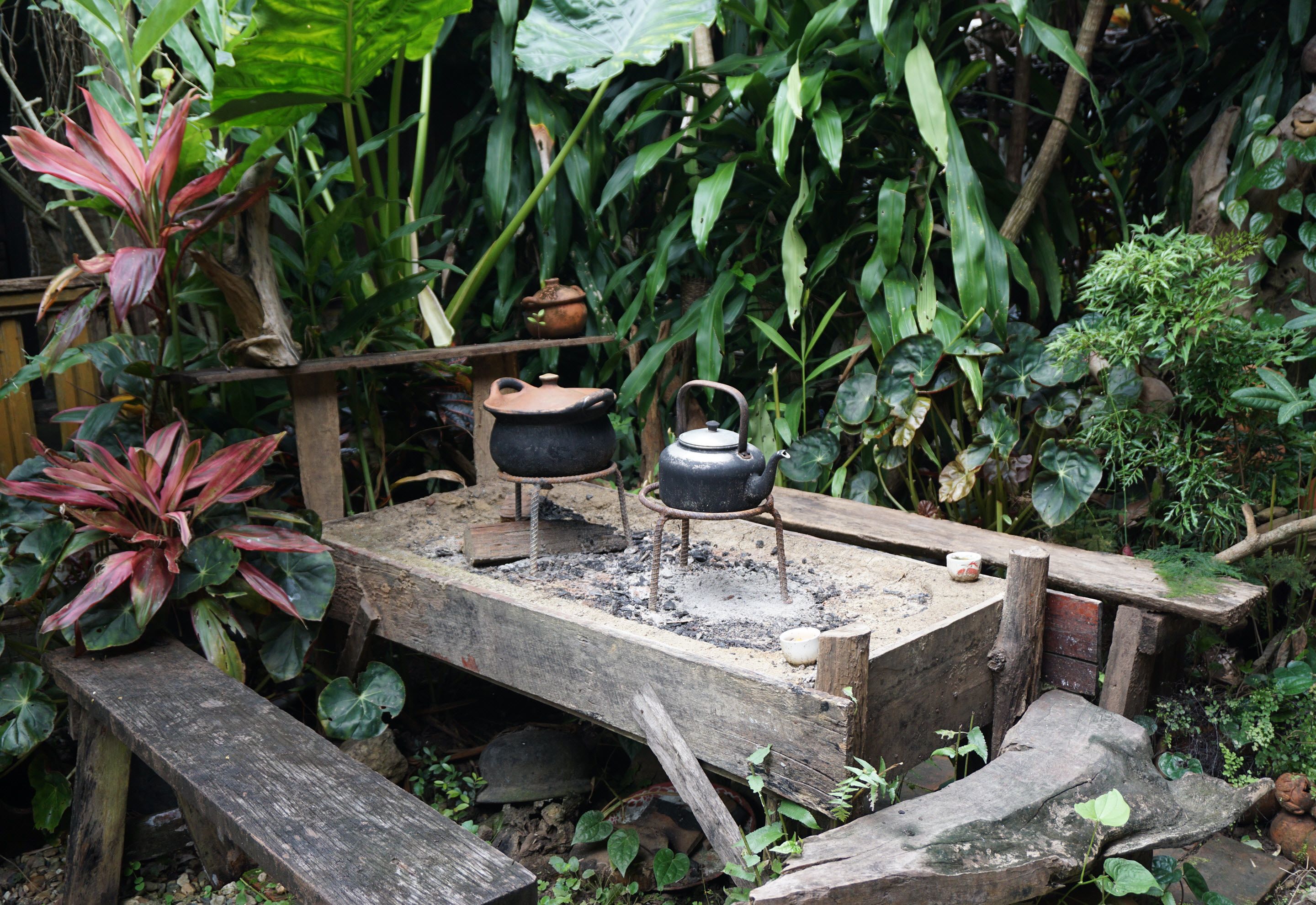 A rustic outdoor cooking area with a wooden table, two pots, and a kettle.