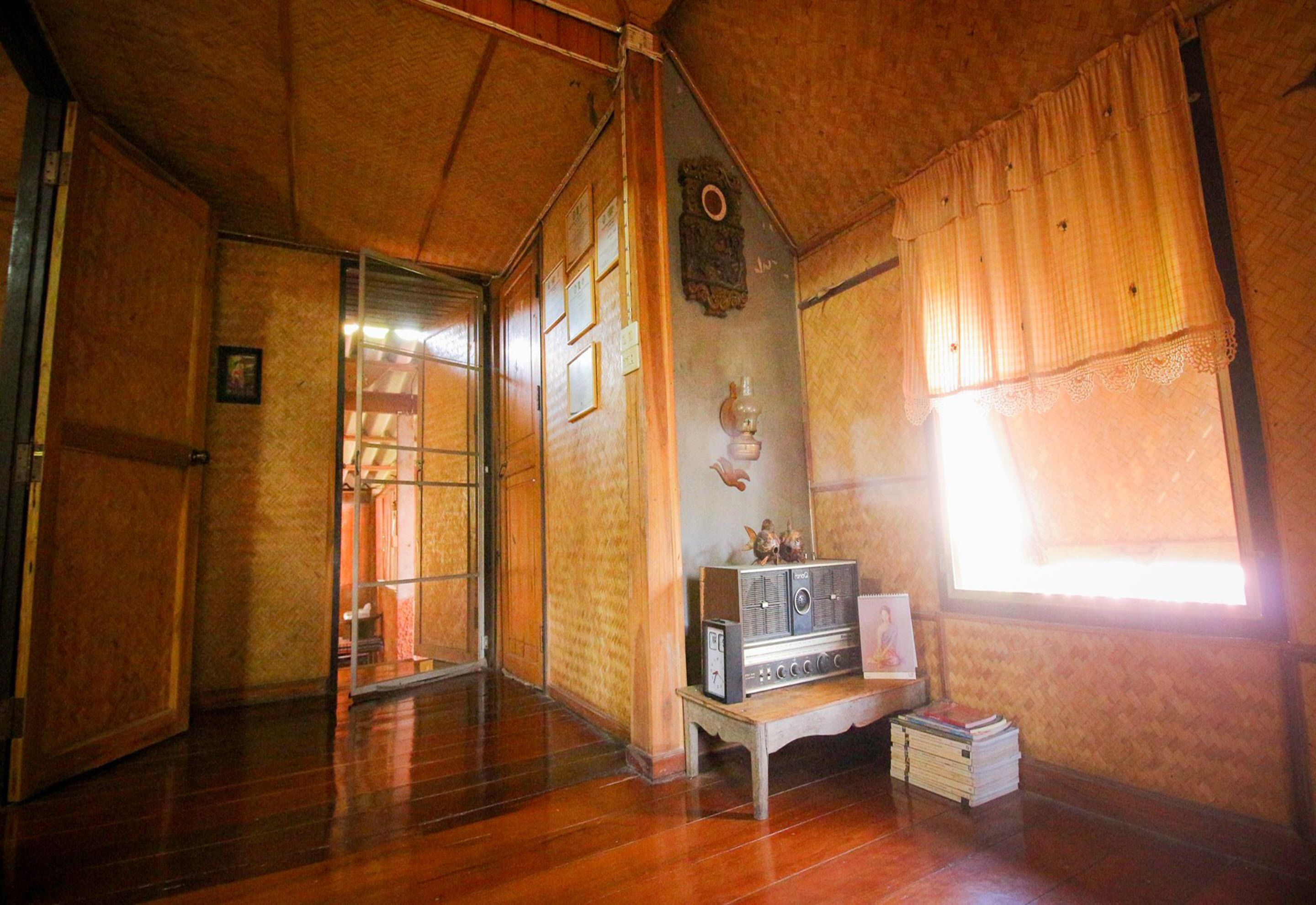 Una habitaci ón de madera con piso de madera, una pequeña mesa con una radio y libros, y una ventana con cortinas.