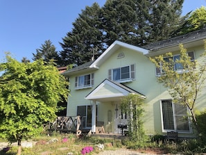 A two-story house with a front porch, a small garden, and a deck. - Guesthouse Chaconne Karuizawa Annex (Karuizawa)