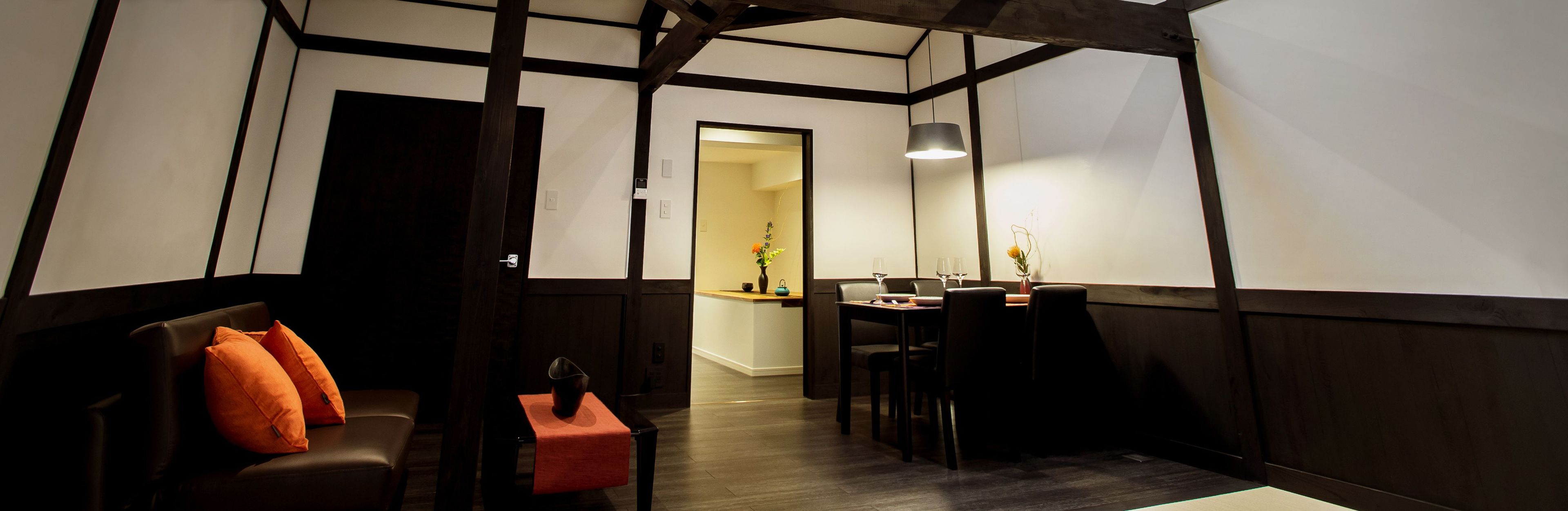 Um quarto com um banco de madeira escura, uma mesa com cadeiras e um lustre.