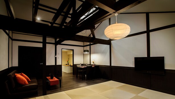 Un intérieur moderne avec un plafond en bois foncé, un coin repas comprenant une table et des chaises, un canapé avec des coussins orange et un téléviseur à écran plat fixé au mur.