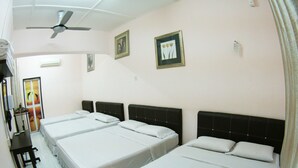 Habitación de hotel con tres camas individuales, un ventilador de techo y ventana con vista al atardecer.