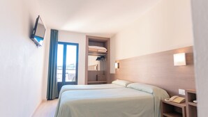 Habitación de hotel con dos camas, un televisor montado en la pared, una mesita de noche con teléfono y vistas a la ciudad a través de la ventana.