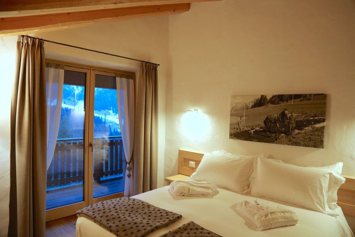 A hotel room with a bed, a nightstand, a painting on the wall, and a sliding glass door leading to a balcony.